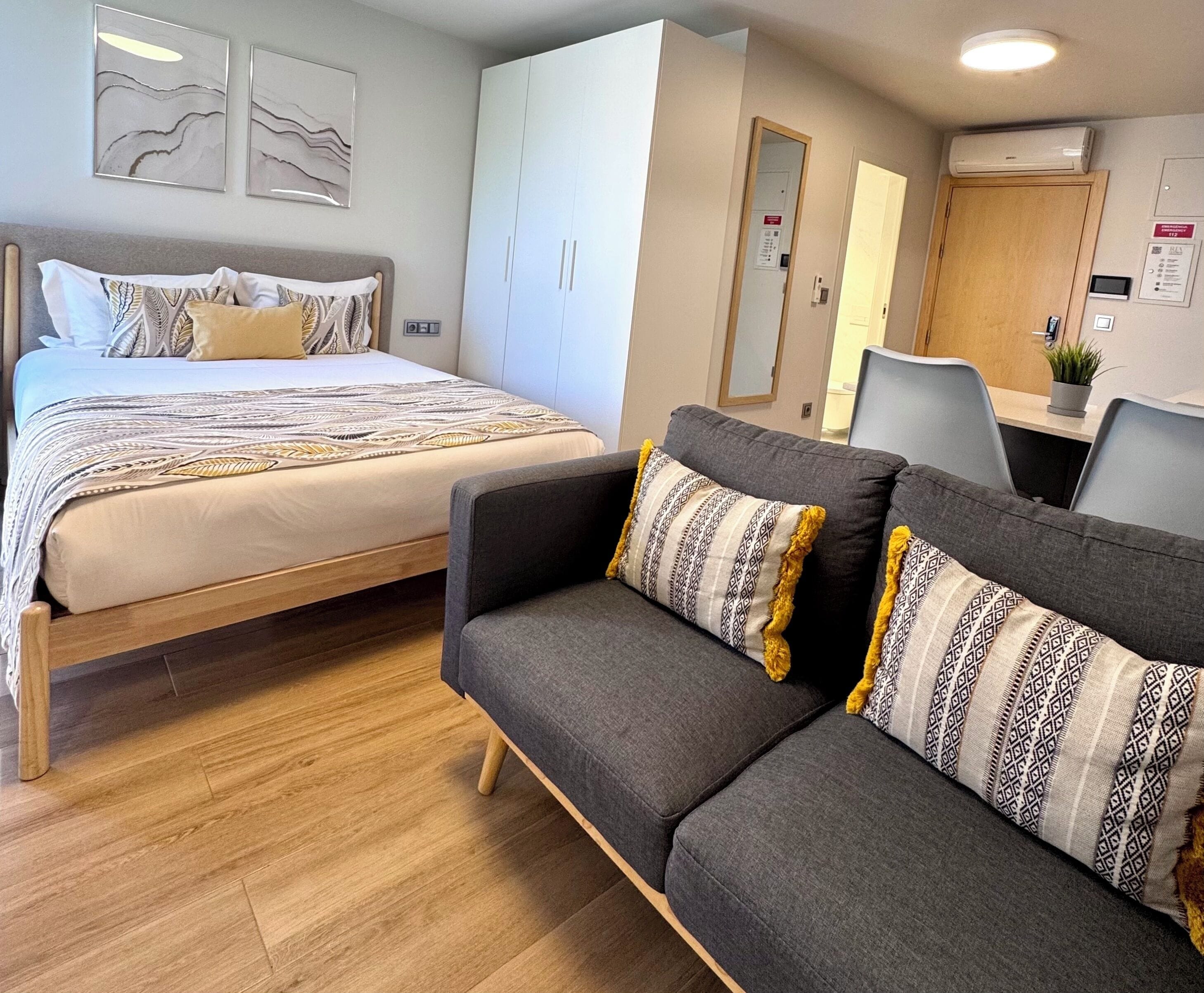 A hotel room with a bed, a sofa, a desk, and a mirror.