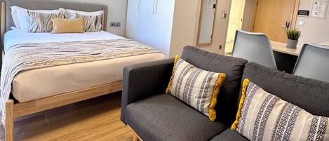 A hotel room with a bed, a sofa, a desk, and a mirror.