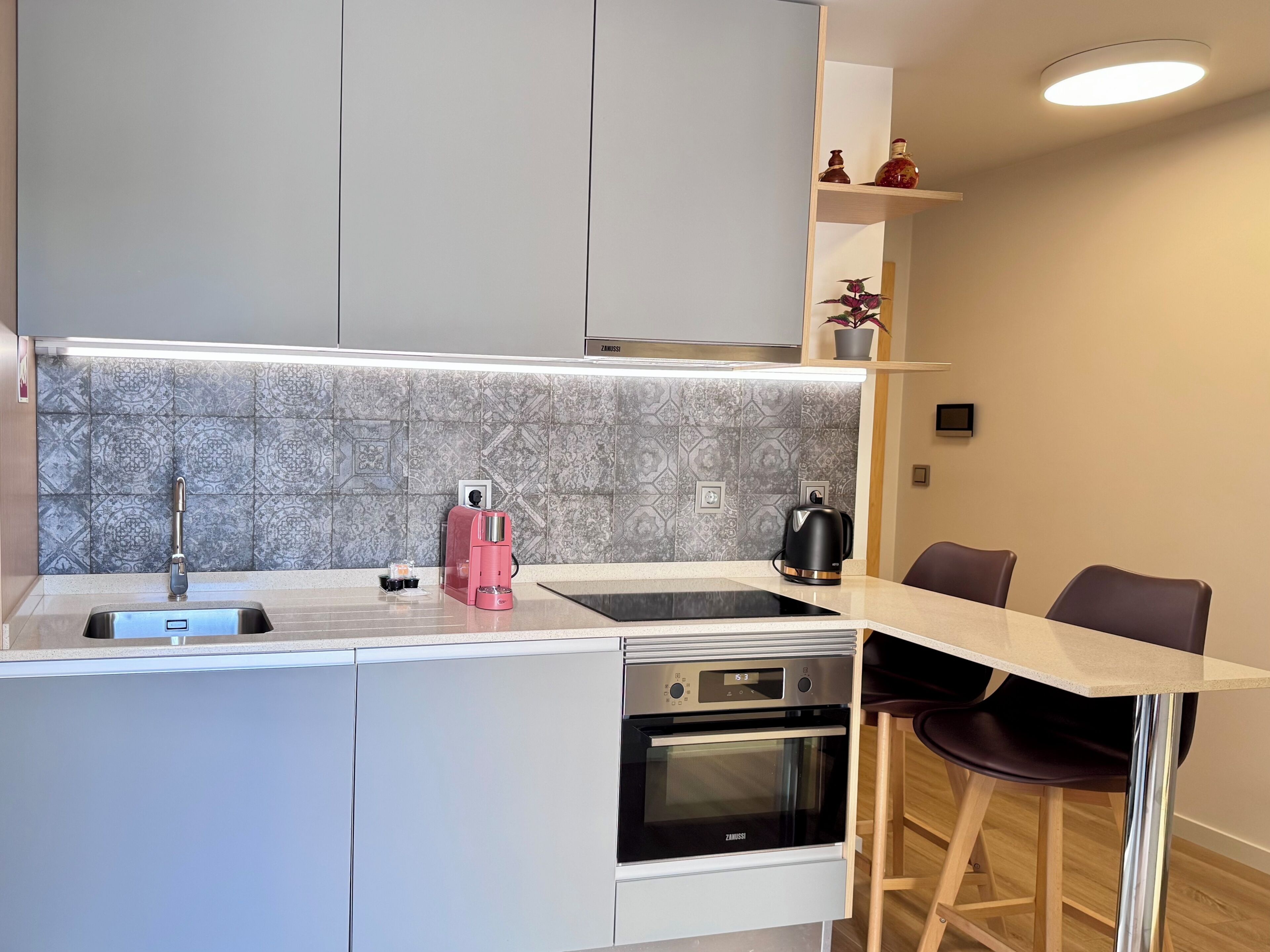 Una cocina compacta con horno empotrado, cafetera y hervidor sobre la encimera.