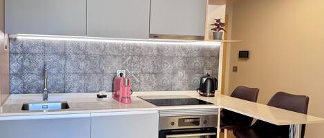 Una cocina compacta con horno empotrado, cafetera y hervidor sobre la encimera.