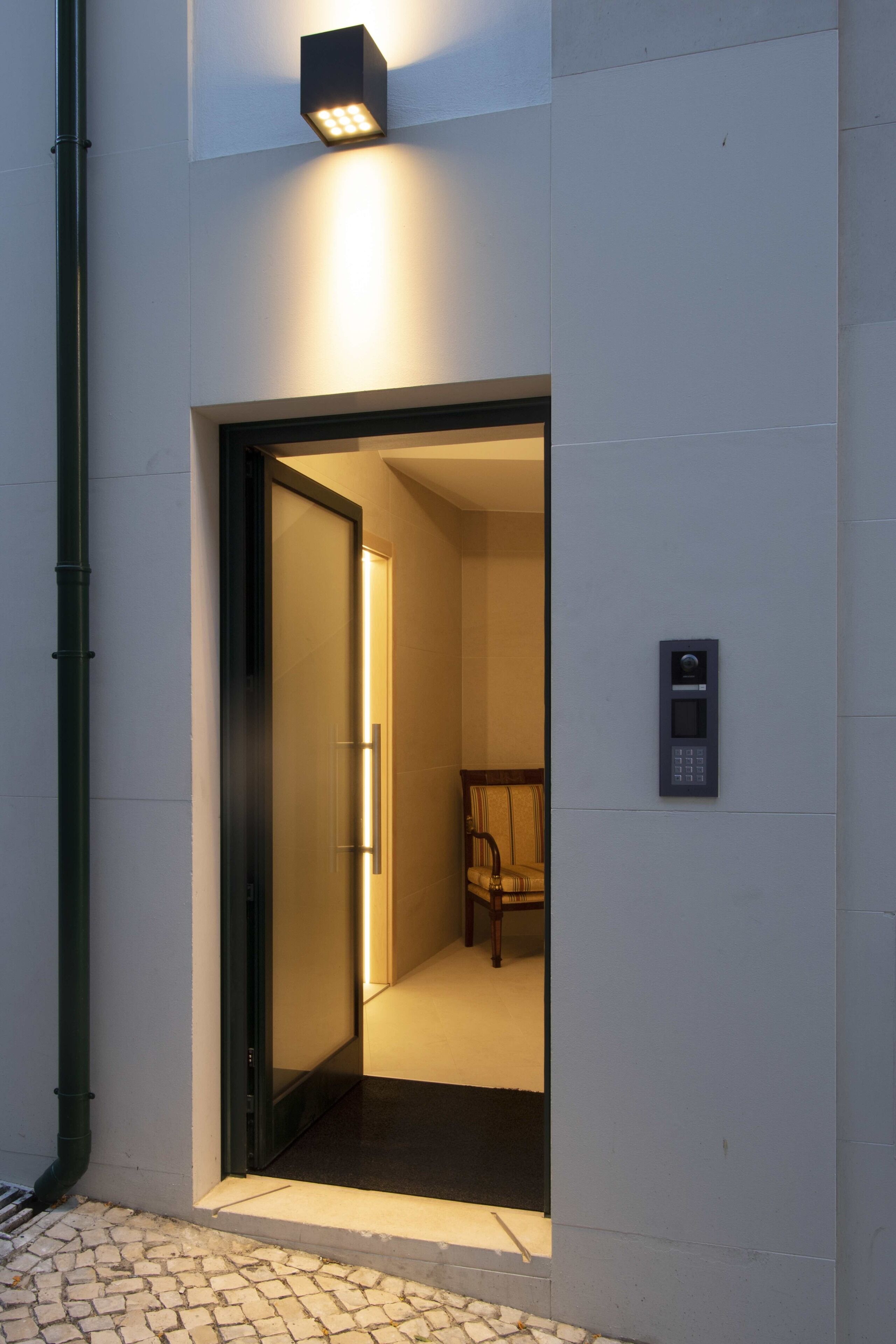 An entrance with a door, a wall-mounted intercom, and a chair inside.