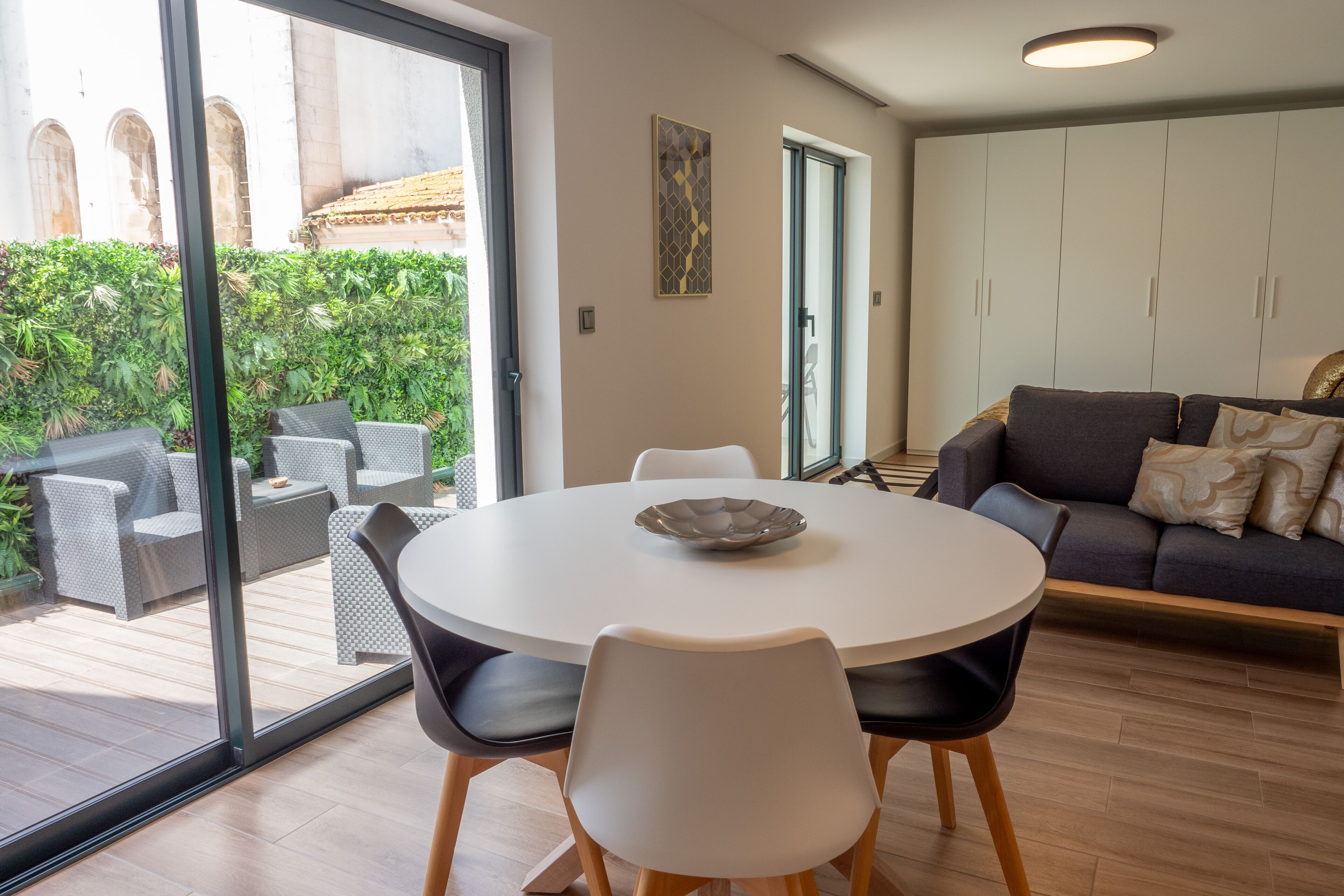 Un salón moderno con una mesa de comedor redonda, sillas blancas y un sofá gris con cojines estampados.