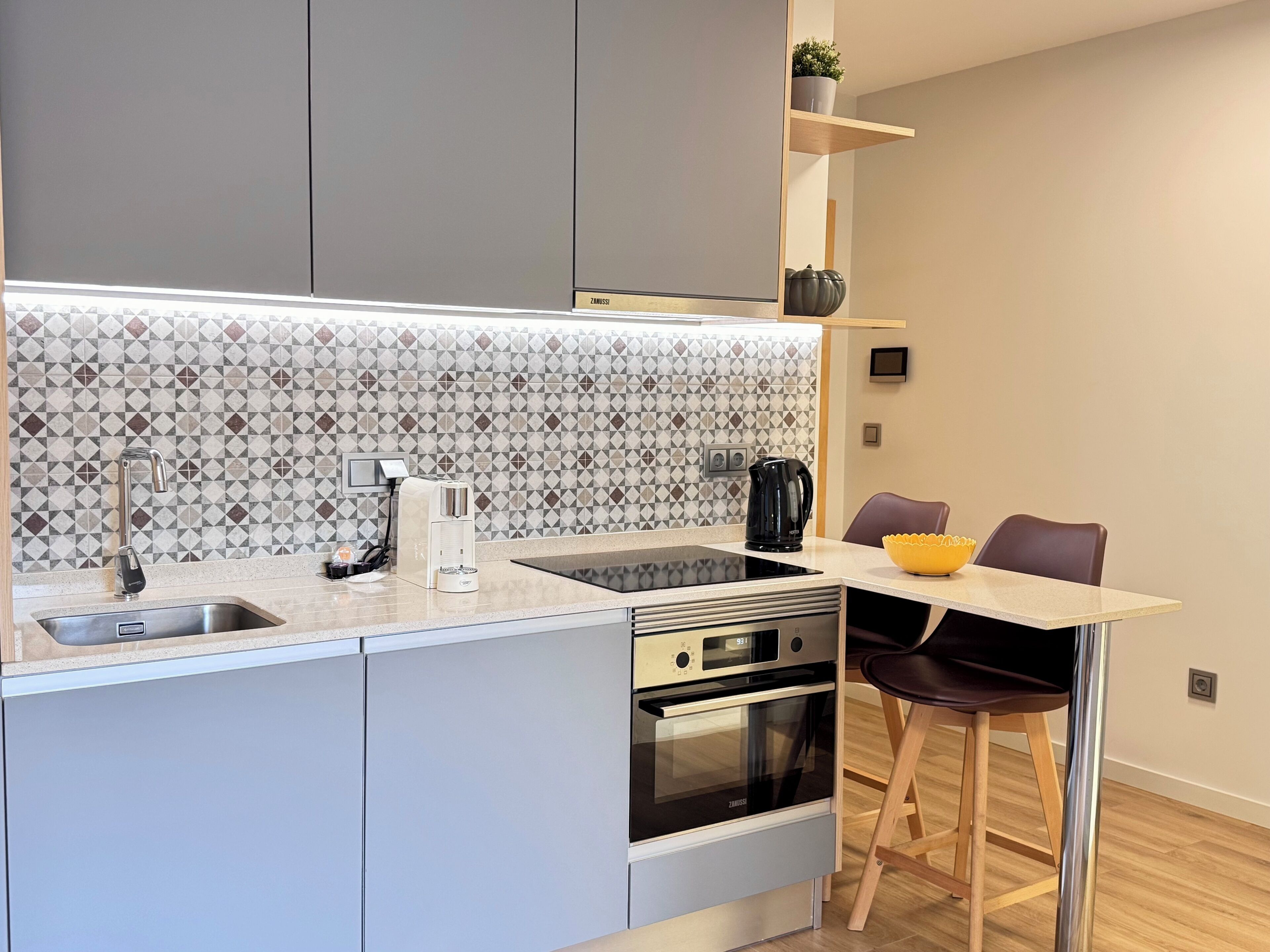 A modern kitchen with a built-in oven, a coffee maker, and a kettle on the counter.