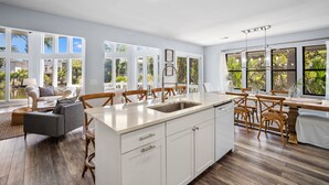 A spacious kitchen with a central island, large windows, and a dining area with wooden chairs. - Wildlife viewers dream! Peaceful & so clean, golf cart incl., pool across street (Fripp Island)