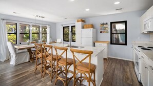 A modern kitchen with white cabinets, a central island with bar stools, a refrigerator, and a microwave. - Wildlife viewers dream! Peaceful & so clean, golf cart incl., pool across street (Fripp Island)