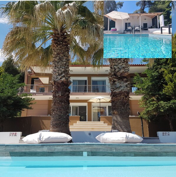 A two-story building with a swimming pool, palm trees, and a covered outdoor seating area.