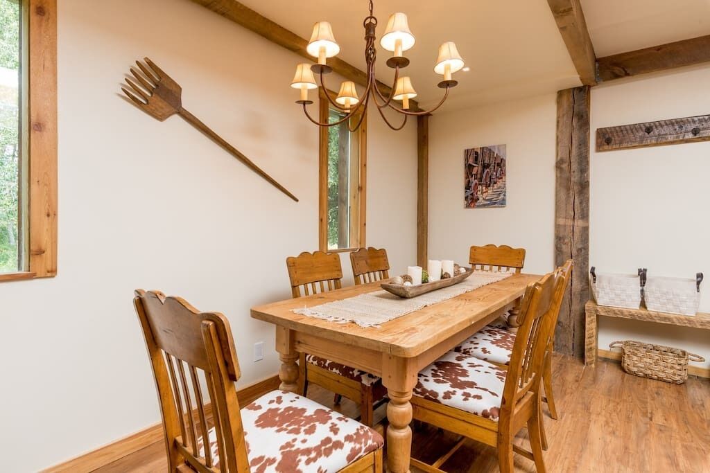 A wooden dining table with six chairs, a chandelier, and a rustic wooden bench with a basket.