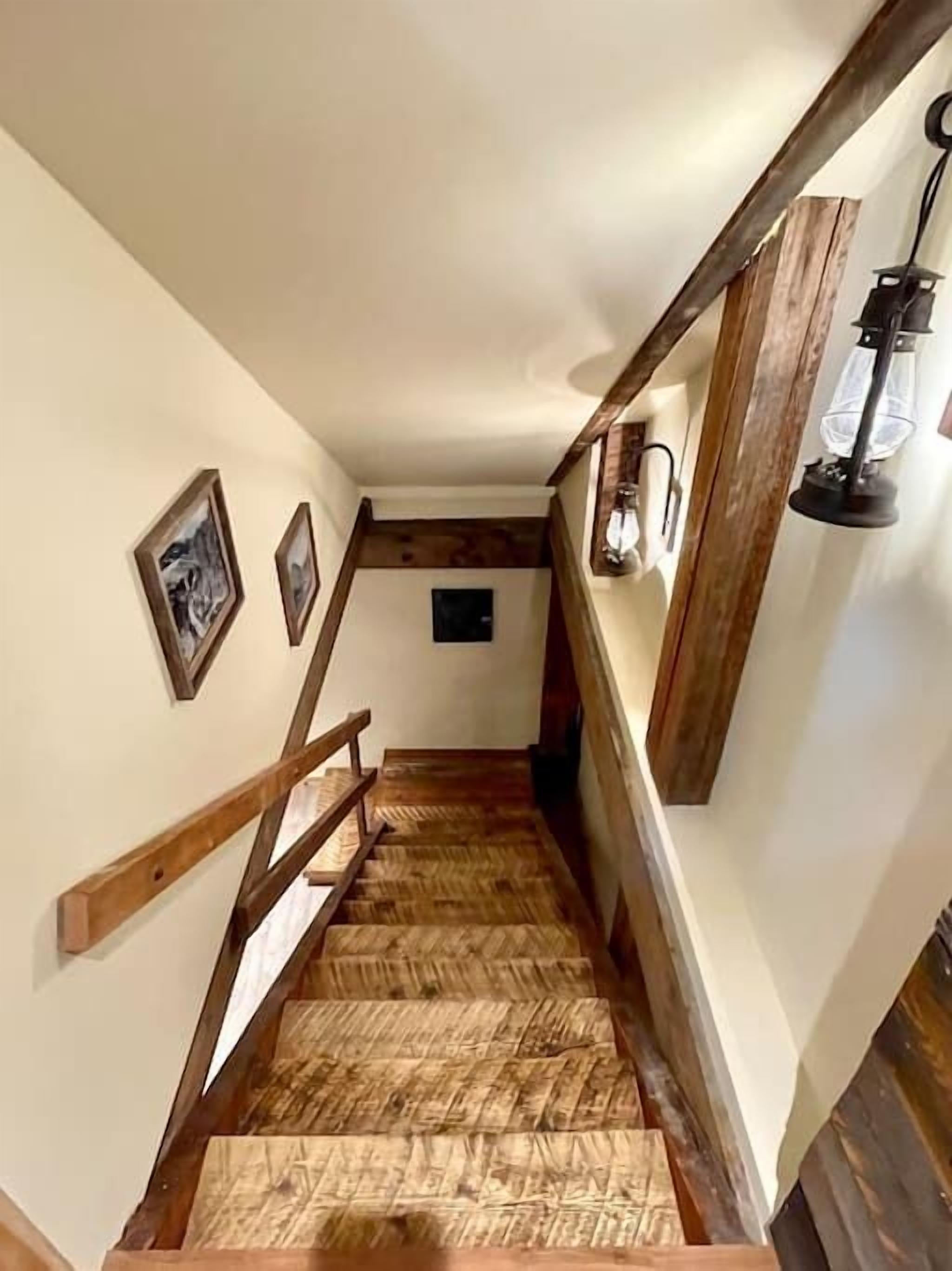 Un escalier en bois avec un revêtement de sol à motifs en chevrons, des rampes en bois et des luminaires fixés au mur.