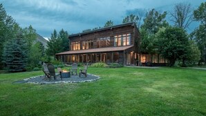 Una casa moderna de dos pisos amb un ampli porxo frontal, una zona de foc i un jardí ben cuidat.