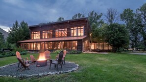 Una casa moderna de dos pisos amb una xemeneia al pati davanter, envoltada de mobles d'exterior.