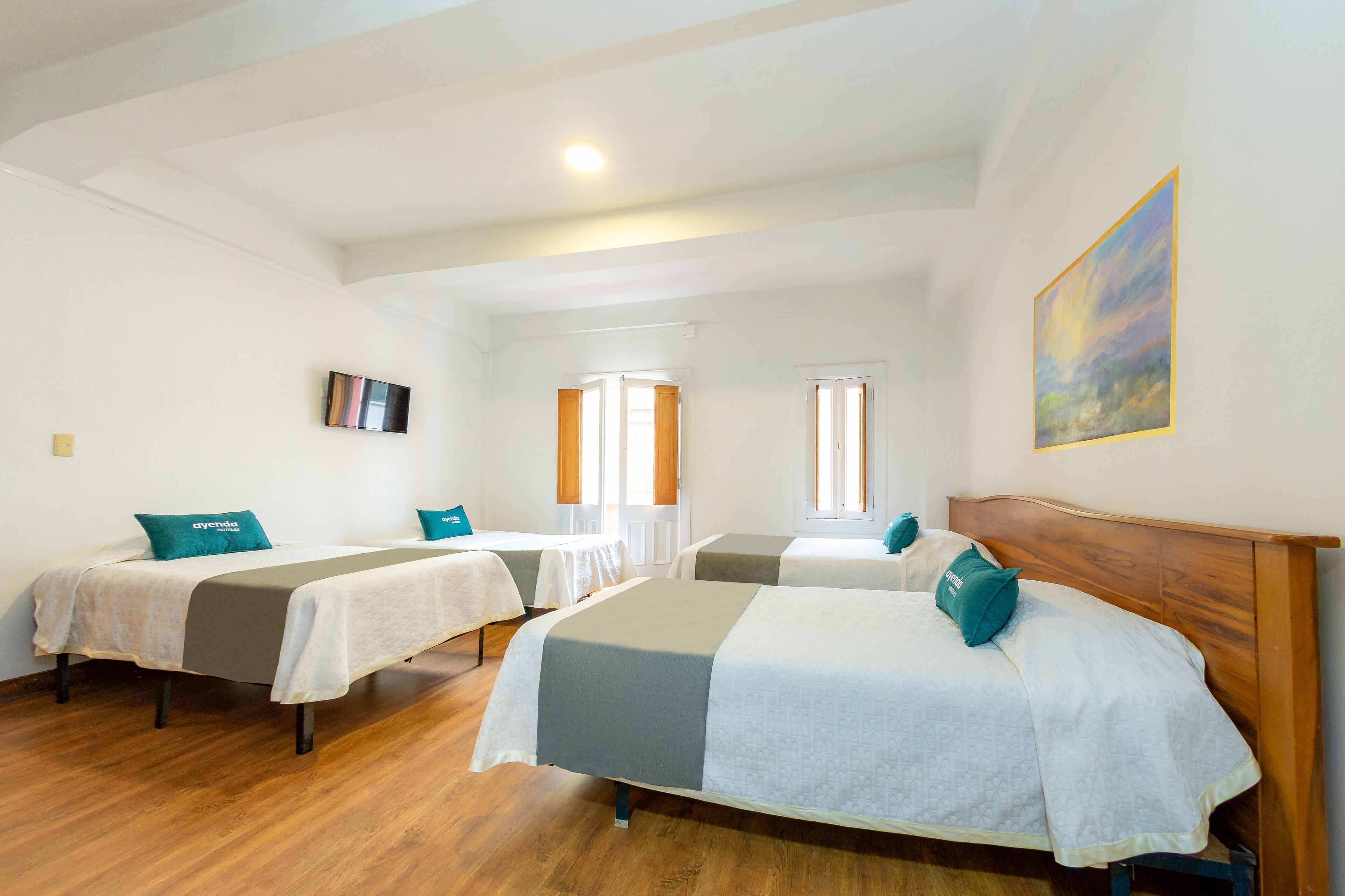 Habitación de hotel con dos camas individuales, piso de madera, un cuadro en la pared y un televisor colgado en la pared.