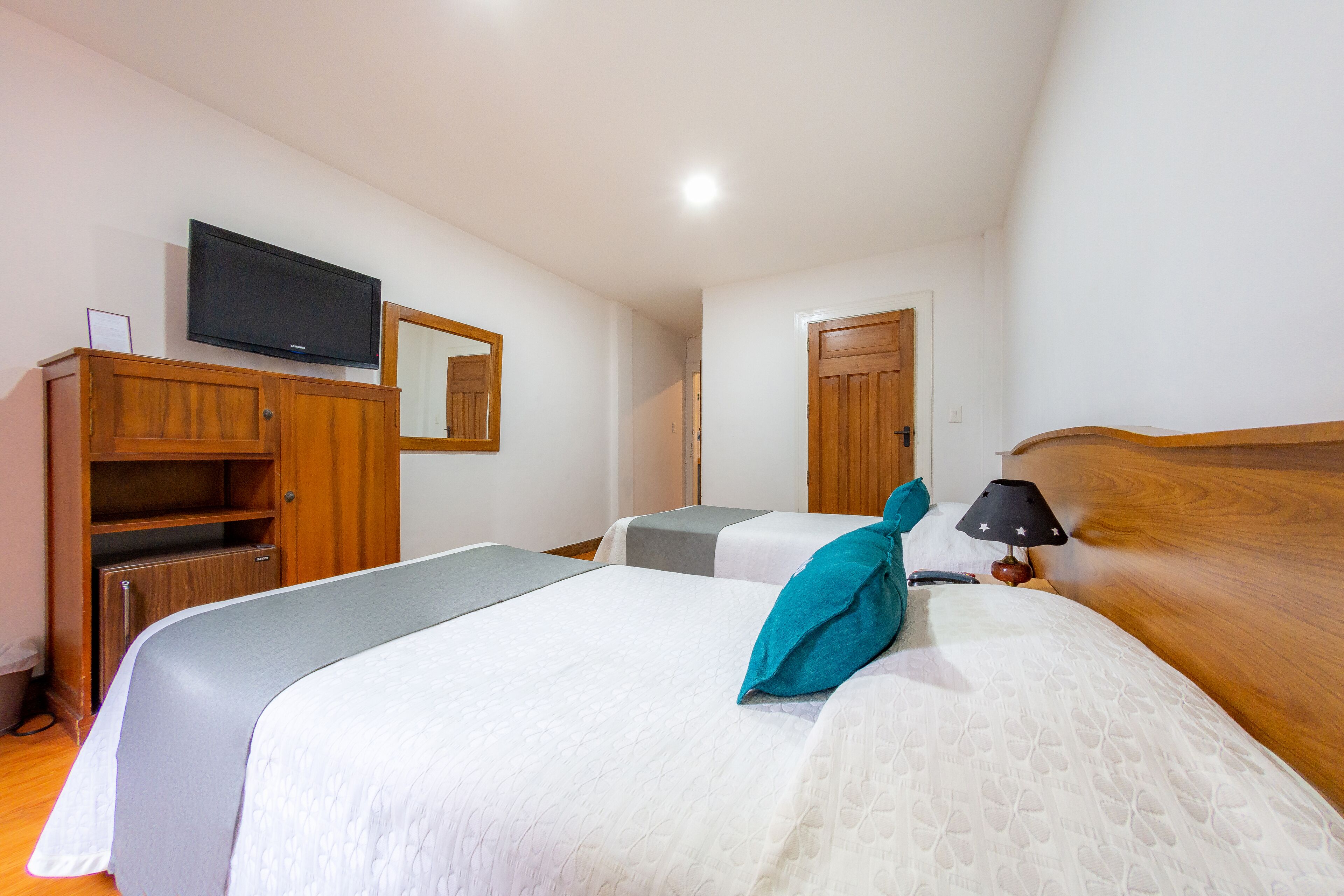 Una camera d'albergo con due letti, una televisione appesa al muro e un armadio in legno.