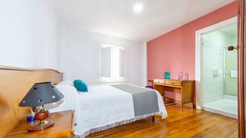 Un dormitorio con cama, mesita de noche, lámpara, escritorio y zona de ducha.