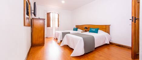 Una habitación de hotel con dos camas, un armario de madera, un televisor montado en la pared y una ventana con cortinas.