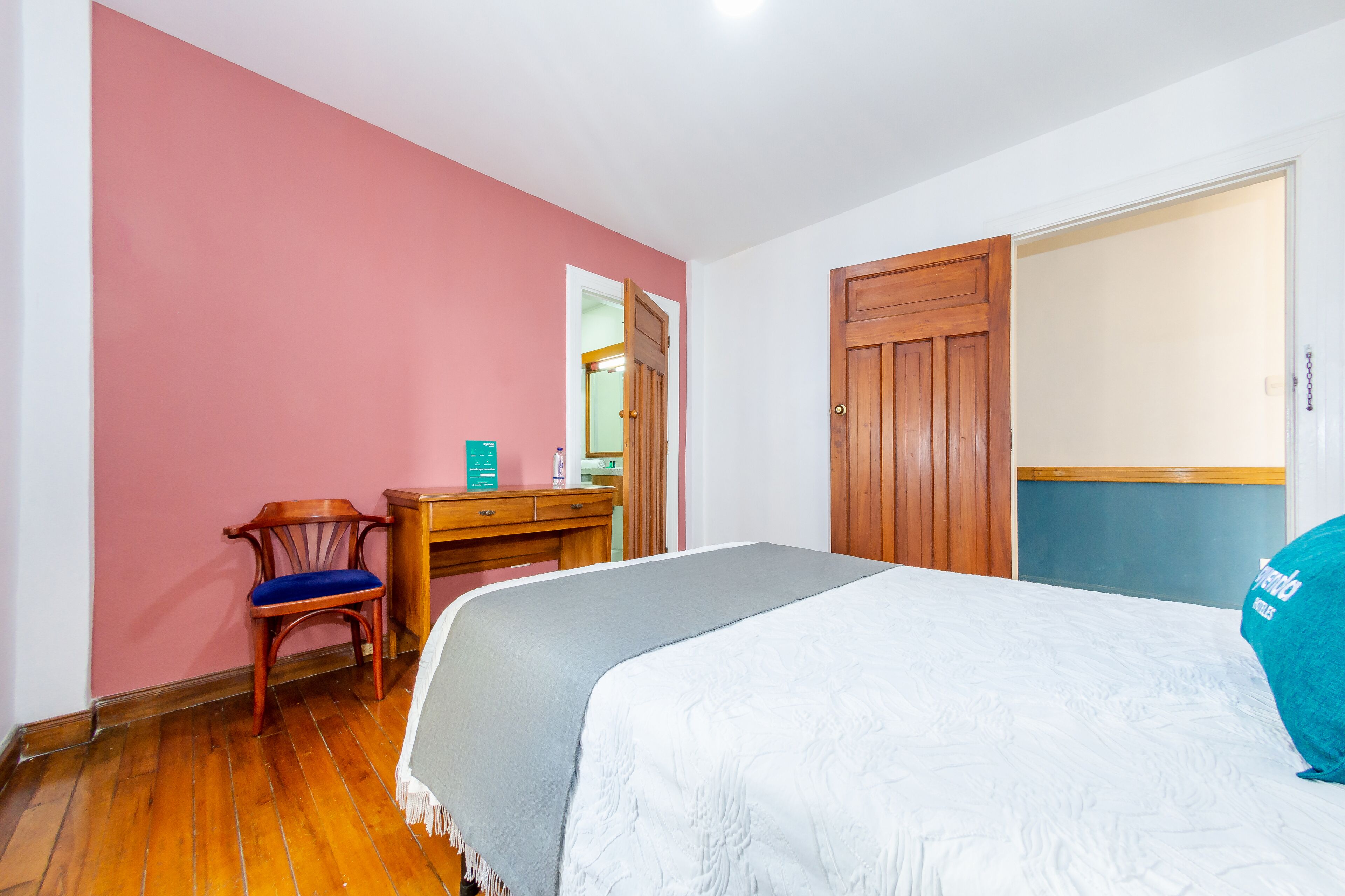 Een slaapkamer met een bed, een houten dressoir, een stoel en een deur.