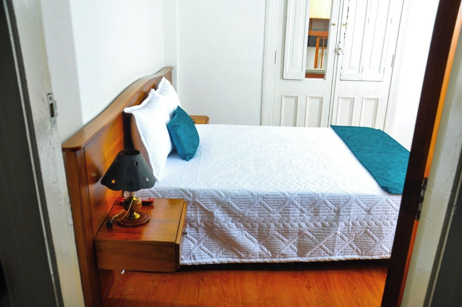 A neatly made bed with a white quilt, a wooden headboard, and a bedside table with a lamp.