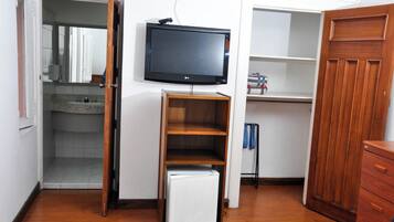 A compact room with a television mounted on the wall, a small refrigerator, and a wooden cabinet.