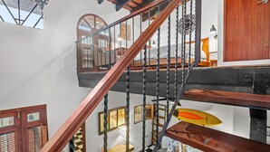 A staircase with a wooden handrail and black balusters, leading to a room with a bed, a desk, and a chair. - Quiet 2BR Loft • Walk Everywhere • King & Queen Beds • Open Layout (San Juan)