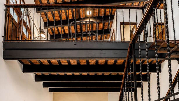 A bedroom with a checkered floor, a bed, a nightstand, a lamp, a bookshelf, and a staircase. - Quiet 2BR Loft • Walk Everywhere • King & Queen Beds • Open Layout (San Juan)