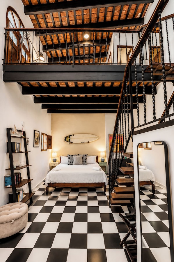 A bedroom with a checkered floor, a bed, a nightstand, a lamp, a bookshelf, and a staircase.
