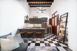 A compact kitchen with a bar stool area, a refrigerator, and a bookshelf.
