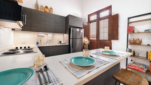 A modern kitchen with dark cabinetry, a central island with teal plates, and a wooden stool. - Quiet 2BR Loft • Walk Everywhere • King & Queen Beds • Open Layout (San Juan)