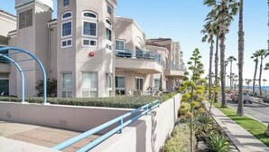 A multi-story hotel with balconies, a blue railing, and a palm tree-lined street. - Comfortable, modern condo located steps from the beach! (Oceanside)