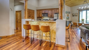 Une cuisine spacieuse avec des meubles en bois, un îlot central doté de tabourets, un coin repas avec un canapé et une grande fenêtre.