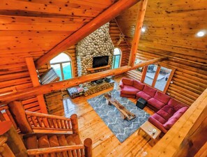 A log cabin interior with a stone fireplace, wooden staircase, and a red sofa. - Beautiful Cabin on a Vineyard (West Branch)
