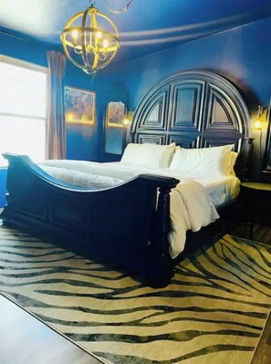 A bedroom with a large bed, a zebra-patterned rug, and a chandelier.