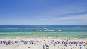 A beach with numerous umbrellas and sun loungers, a clear blue sky, and the ocean.