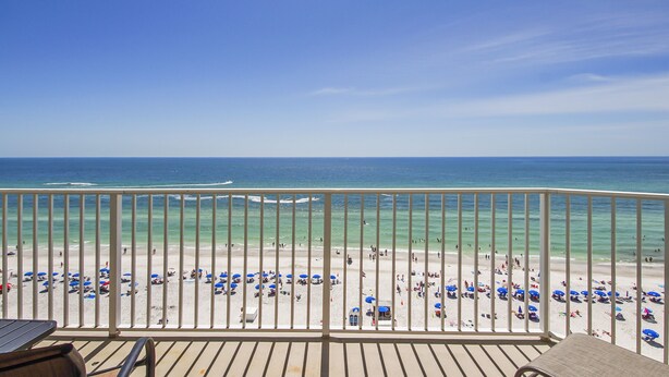 A balcony with a view of a beach with people and umbrellas.