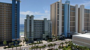 A high-rise hotel with multiple balconies, a parking area, and a view of the beach.