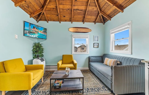 A living room with a wooden ceiling, a TV, a plant, a sofa, a coffee table, and a window with a view.