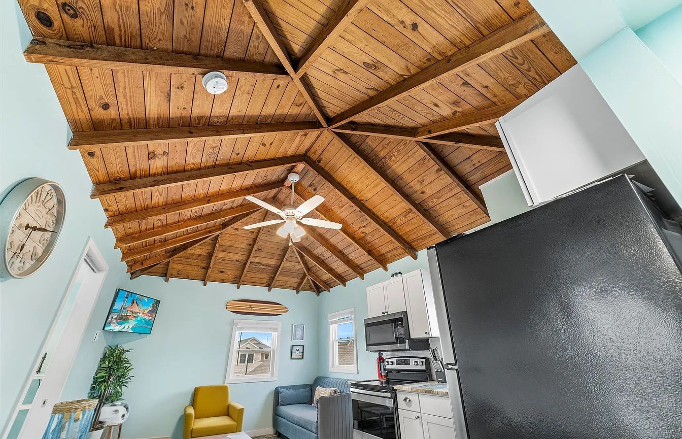 A kitchen with a black refrigerator, wooden ceiling beams, a ceiling fan, and a microwave.