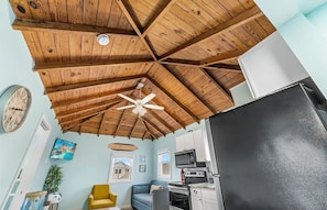 A kitchen with a black refrigerator, wooden ceiling beams, a ceiling fan, and a microwave.