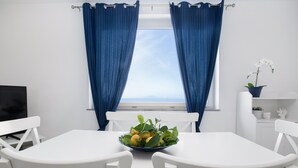 Ein Zimmer mit einem weißen Tisch und Stühlen, einer Obstschale, einer Topfpflanze und einem Fernseher auf einem Schrank.