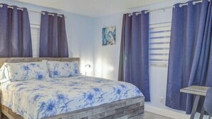 Una camera da letto con struttura letto in legno, copriletto floreale e vista sull'esterno tramite una finestra con tende.