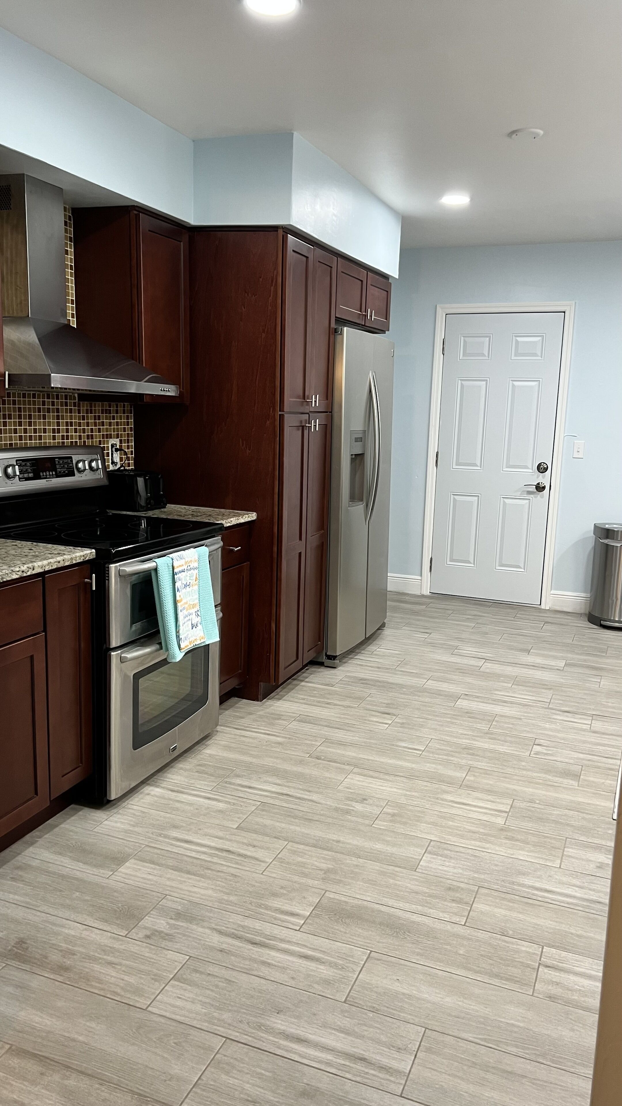 Una cocina moderna con armarios de madera oscura, electrodomésticos de acero inoxidable y piso con diseño en espiga.