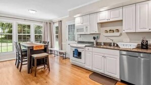 A kitchen with white cabinets, a dining table with chairs, and a dishwasher. - Beautiful Home Walking Distance to Elon University (Elon)