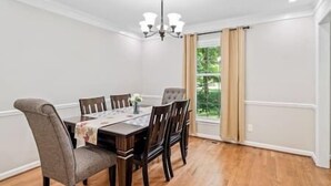 A dining room with a wooden table, six chairs, a chandelier, and a window with curtains. - Beautiful Home Walking Distance to Elon University (Elon)