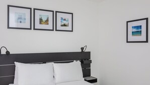 A neatly made bed with white linens, a black headboard, and a bedside table with a lamp. Three framed pictures are hung on the wall above the bed. - Centrally Located 1BD Flat in the Heart of London (London)