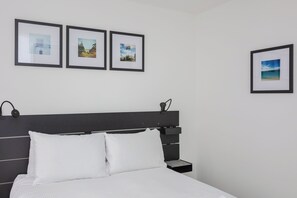 A neatly made bed with white linens, a black headboard, and a bedside table with a lamp. Three framed pictures are hung on the wall above the bed. - Centrally Located 1BD Flat in the Heart of London (London)