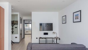 En moderne stue med en grå sofa, et fjernsyn ophængt på væggen og et lille bord med en lampe.