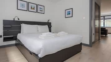A modern bedroom with a large bed, a bedside table, and a headboard. There are three framed pictures on the wall.