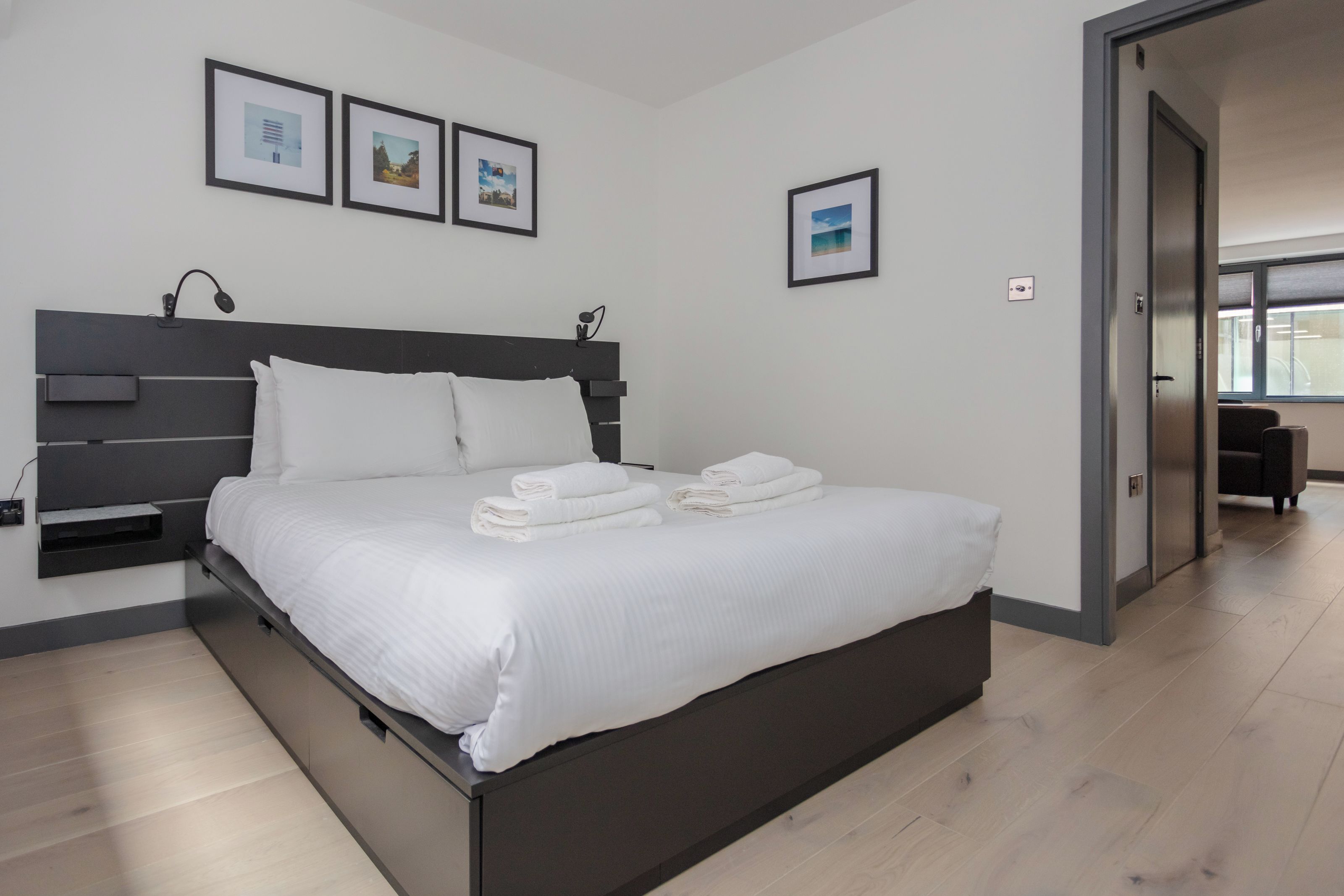 Una camera d'hotel moderna con un letto grande, un comodino e una lampada a parete. Sono presenti tre quadri appesi al muro.