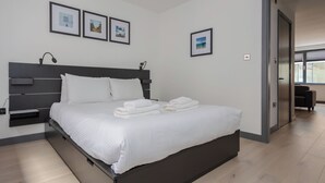 A modern hotel room with a large bed, a bedside table, and a wall-mounted lamp. There are three framed pictures on the wall. - Centrally Located 1BD Flat in the Heart of London (London)