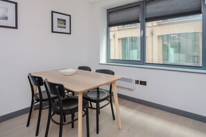 A modern room with a wooden table and black chairs, a window with blinds, and a wall-mounted air conditioner. - Centrally Located 1BD Flat in the Heart of London (London)