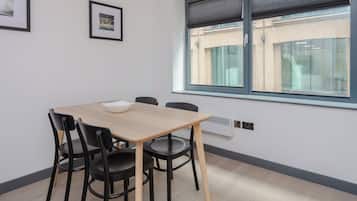 A room with a wooden table, four black chairs, a white bowl, two framed pictures on the wall, and a window with a view of a brick building.