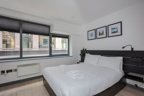 Een moderne hotelkamer met een groot bed, een raam met zonwering, een nachtkastje en een wandlamp.